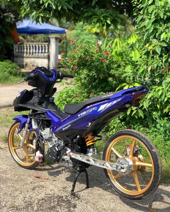 a blue and gold motorcycle parked on the side of a dirt road next to trees