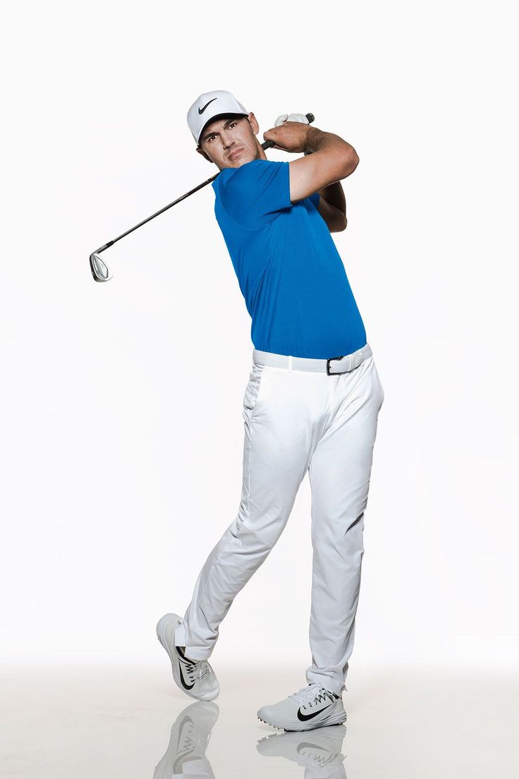 a man in blue shirt and white pants hitting a golf ball with a club on his shoulder