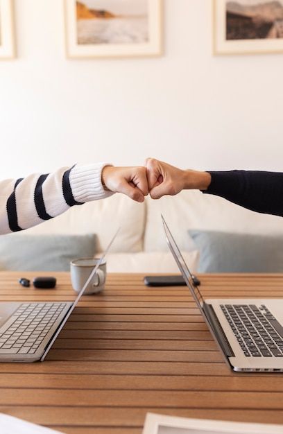 two people shaking hands over a laptop computer on a wooden table in front of a couch