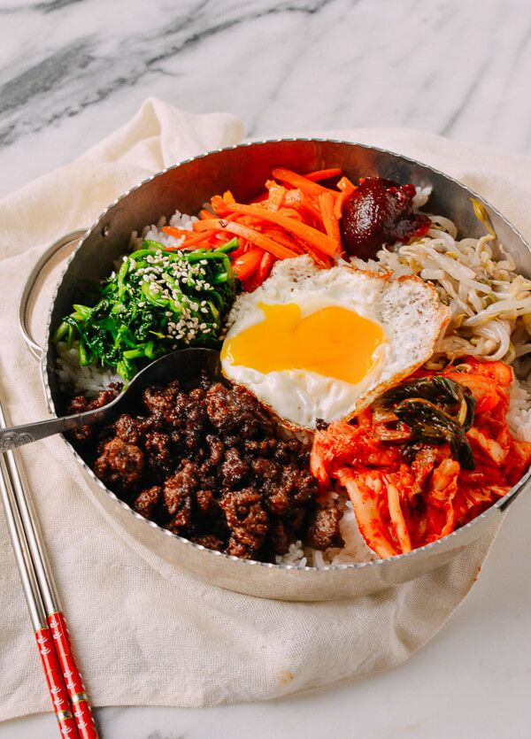 a pan filled with meat, vegetables and an egg on top of rice next to a fork