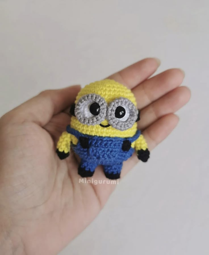 a small crocheted yellow and blue minion with big eyes sitting in someone's hand