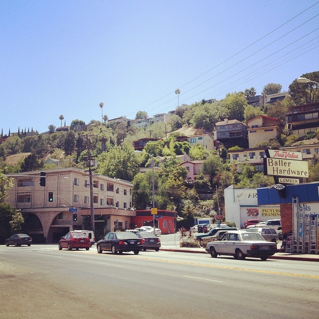 several cars are driving down the street in front of buildings on a hill with palm trees