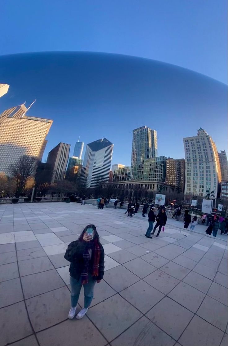 a person standing in front of a large metal object with buildings in the back ground