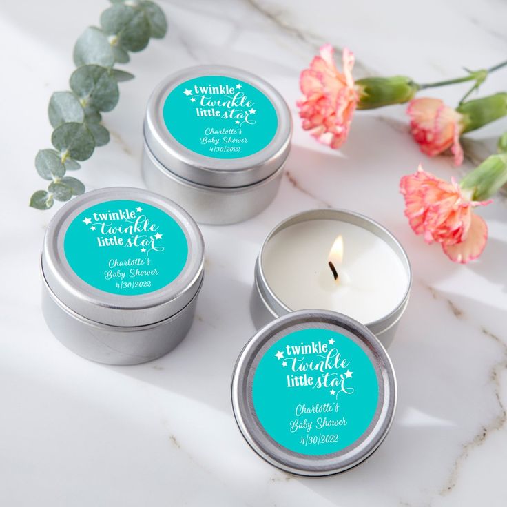 three tins with candles and flowers on a marble countertop next to each other