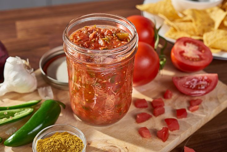 a wooden cutting board topped with a jar filled with chili sauce and veggies