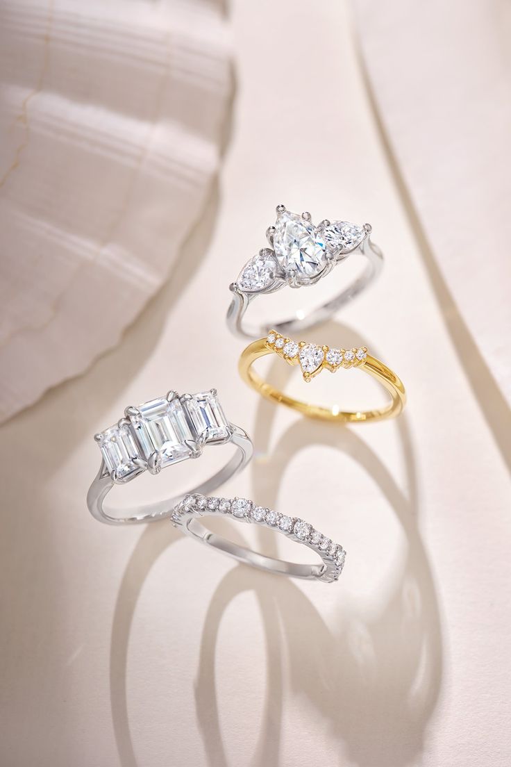 three different rings with diamonds on them sitting next to each other in front of a white cloth