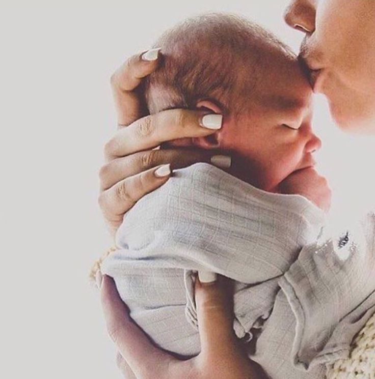 a woman holding a baby in her arms and kissing it's face with the other hand