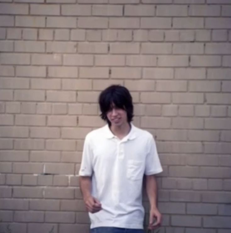 a young man standing in front of a brick wall