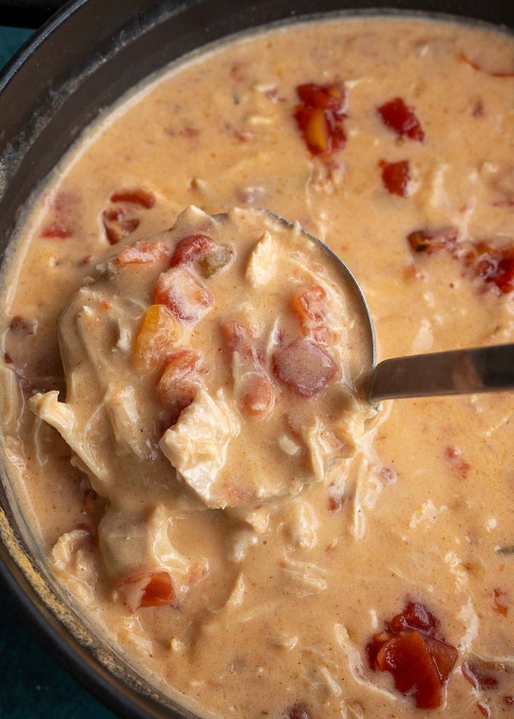 a ladle full of soup with meat and cheese in it, being stirred by a spoon