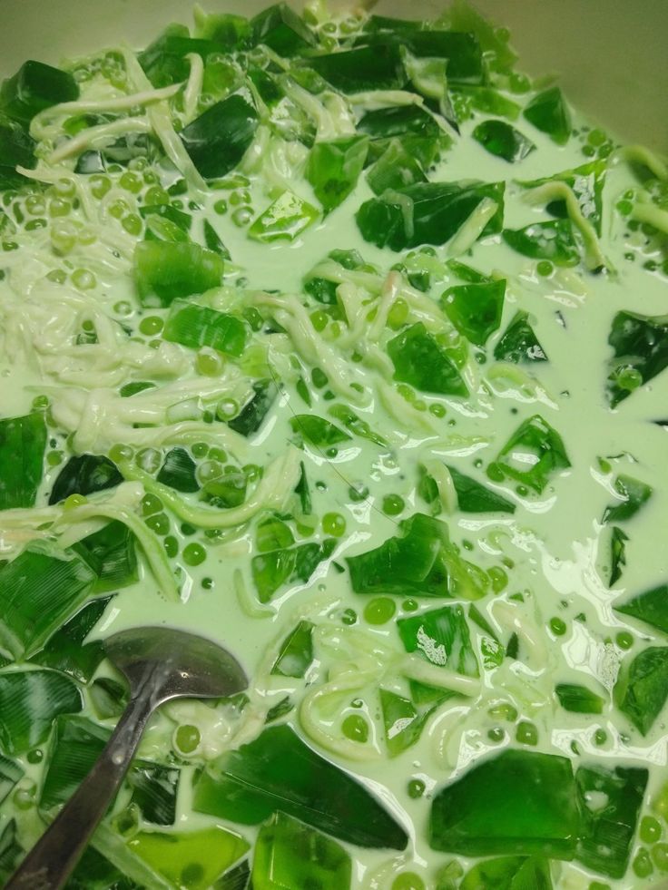 green vegetables being cooked in a pan with spoons and sauce on the side,