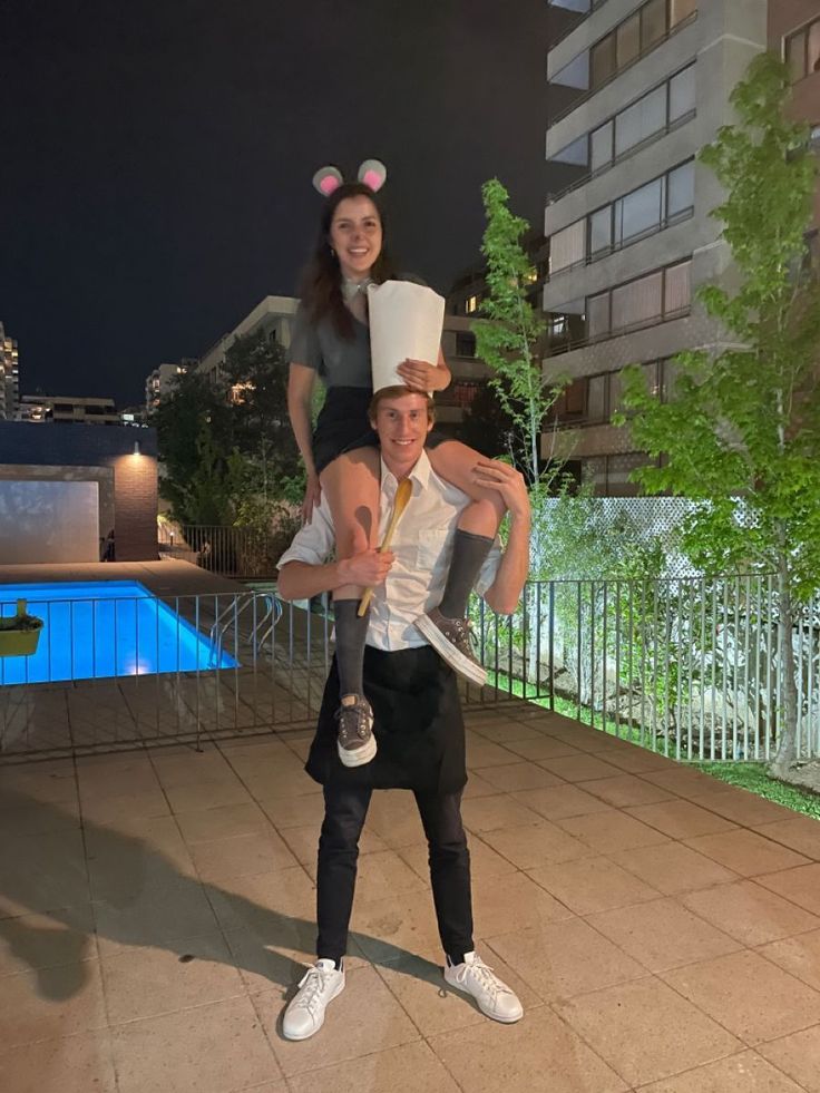 a man holding a woman on his shoulders while standing in front of a pool at night