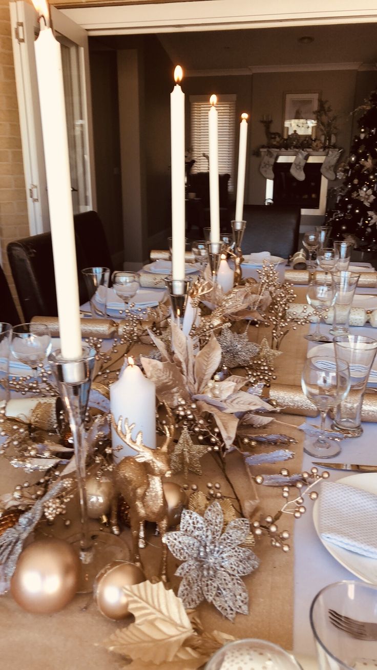 a dining room table set for christmas with silver and gold decorations on the centerpiece