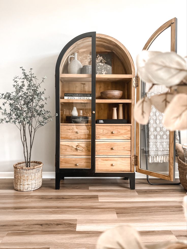 a wooden cabinet sitting on top of a hard wood floor next to a potted plant