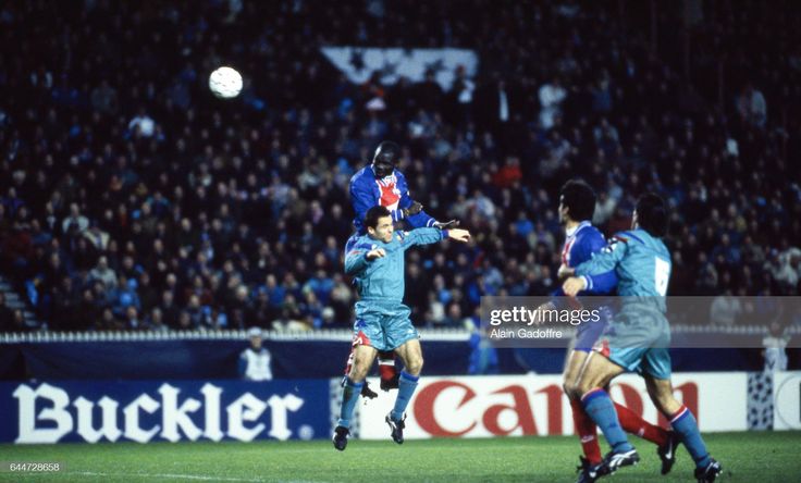 two soccer players jump to head the ball in front of an audience during a game