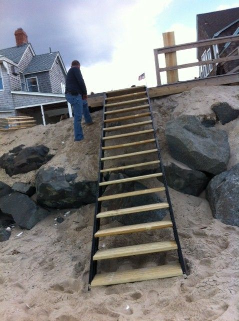 a man standing on top of a sandy beach next to a set of stairs that are made out of wood