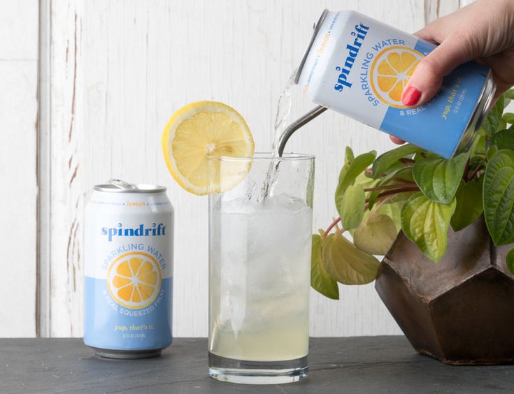 a person pouring lemonade into a glass next to a potted plant and a can