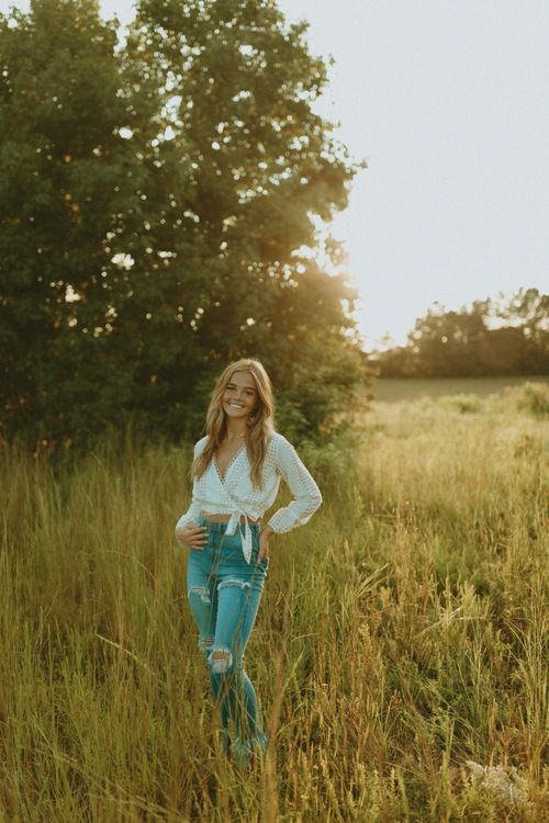 a woman standing in tall grass with her hands on her hips