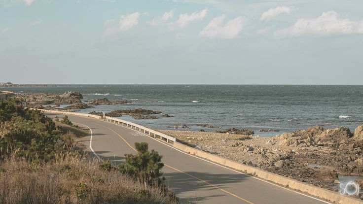 an empty road next to the ocean on a sunny day