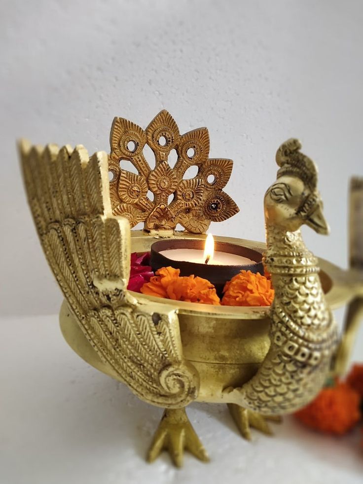 a golden peacock shaped candle holder sitting on top of a white table next to orange pom poms