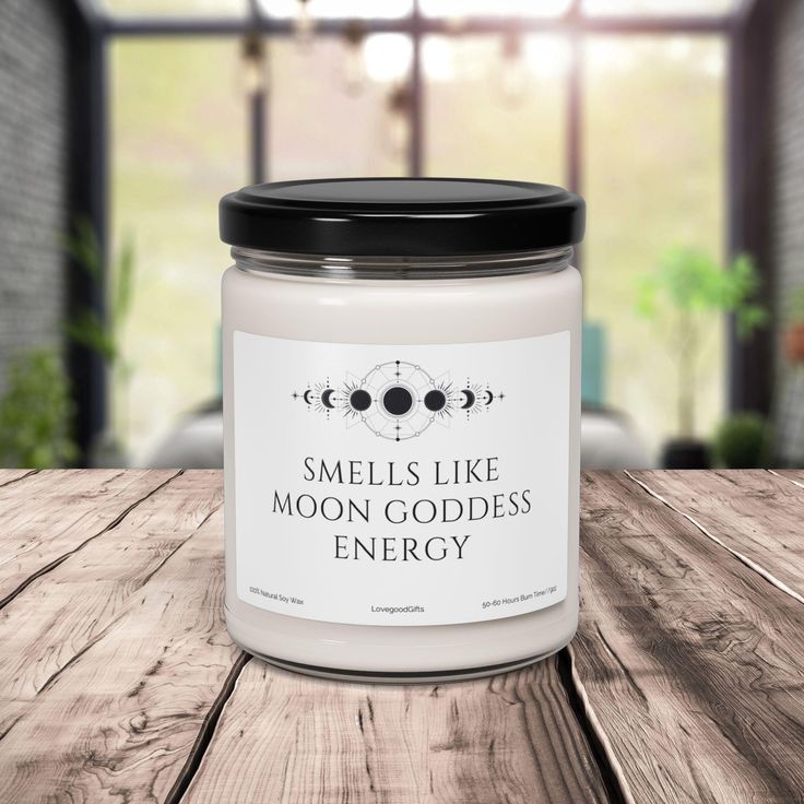 a candle that says smells like moon goddess energy sitting on a wooden table in front of an open window