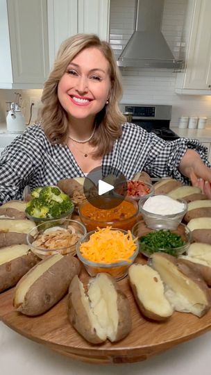 a woman sitting in front of a wooden platter filled with different types of food