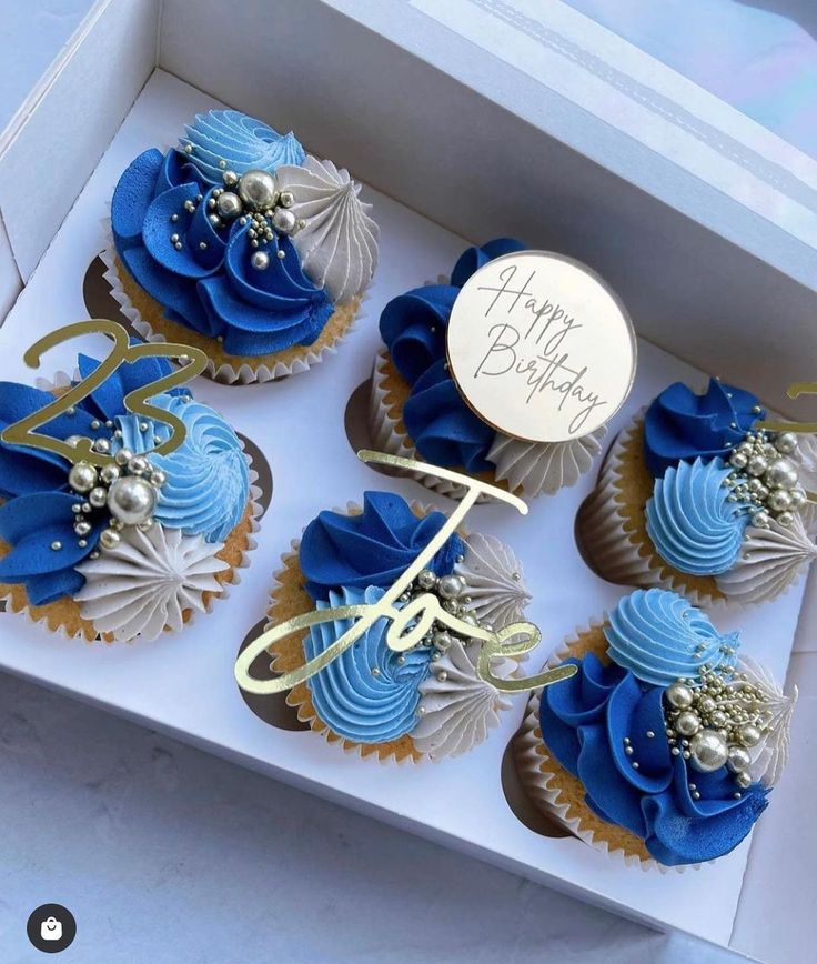 blue and gold cupcakes in a box with a happy birthday sign on top