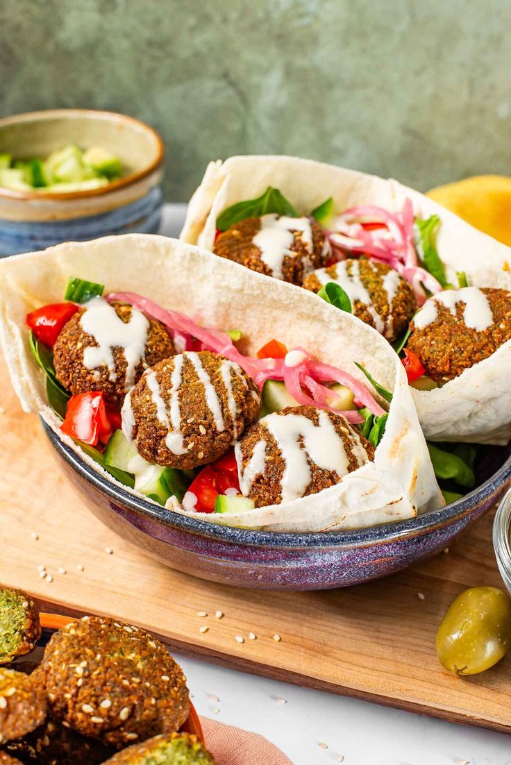 two pita breads with meat and vegetables on a cutting board next to olives