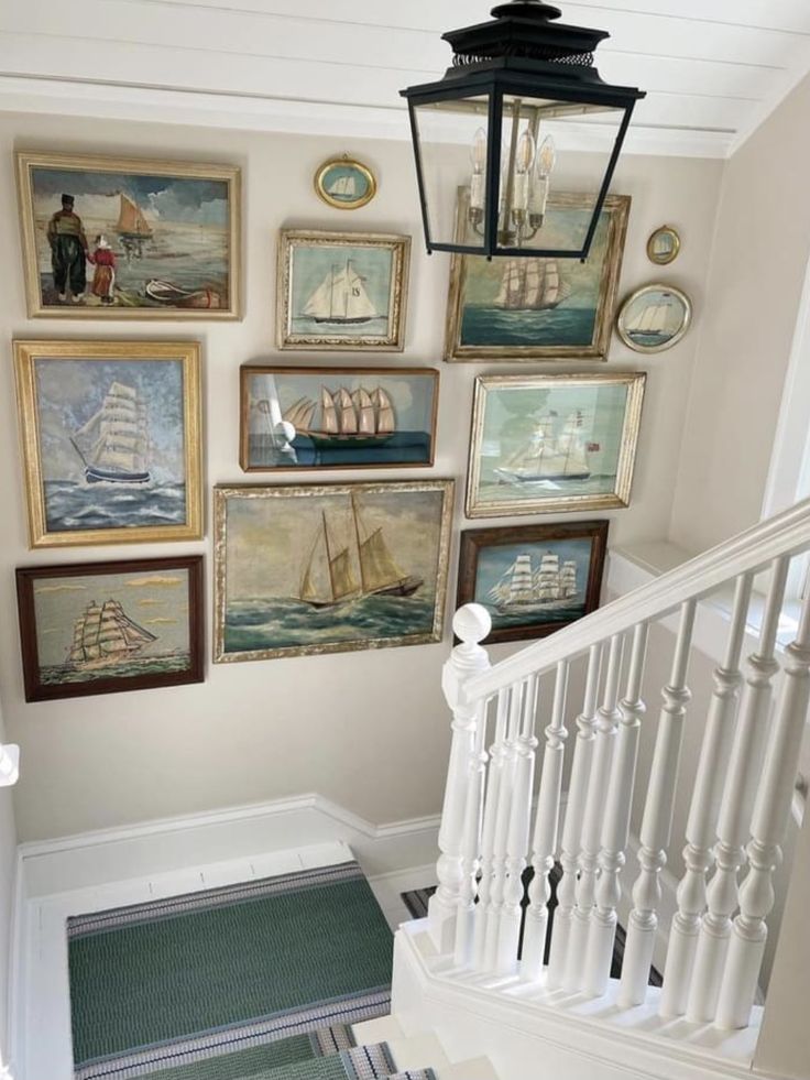 there are many pictures on the wall above the stairs in this house, including sailboats and lighthouses