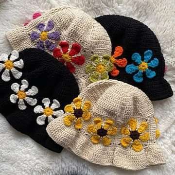 four hats with crochet flowers on them sitting on a white surface, one is black and the other has multicolored daisies