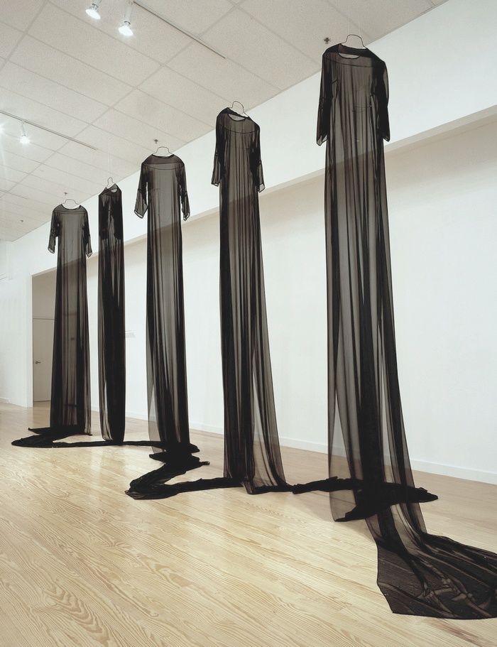 four black sheer dresses are on display in an empty room with wooden floors and white walls