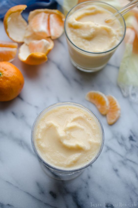 two glasses filled with cream sitting on top of a table next to sliced oranges