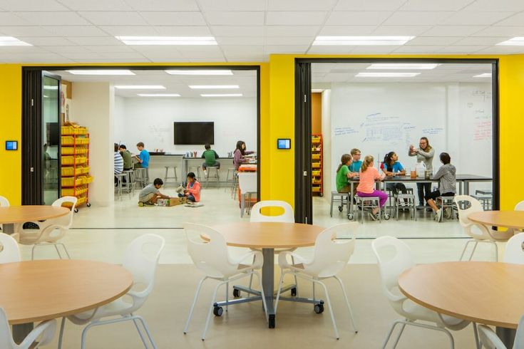 people are sitting at tables in an open room with yellow walls and white flooring