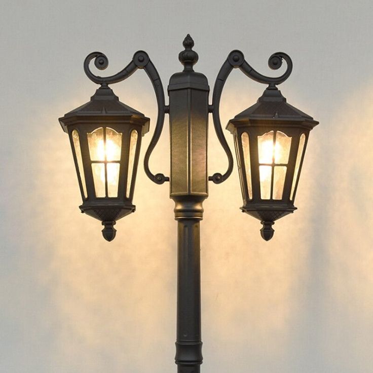 an old fashioned street lamp with two lights on it's sides, against a white wall