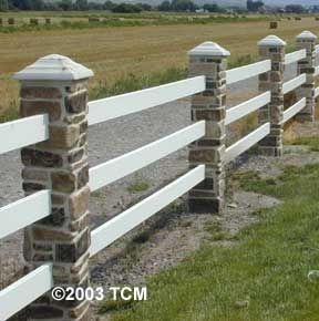 a white fence with stone pillars and posts in front of an open field on a sunny day