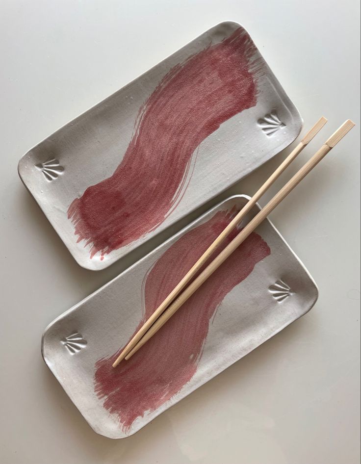 two plates with chopsticks on them that have red liquid painted on them and are sitting next to each other