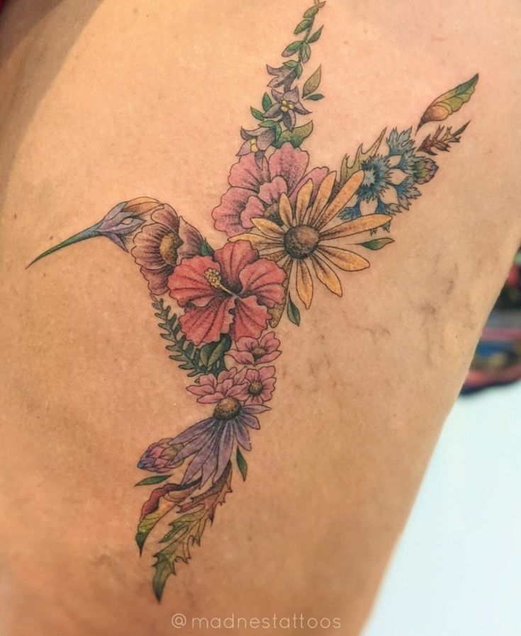 a hummingbird with flowers on its back is shown in this tattoo artist's photo