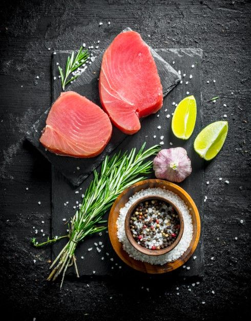 raw fish fillets with herbs and spices on black slate board