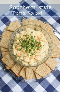 a plate with crackers, cheese and green garnish in it on a checkered table cloth