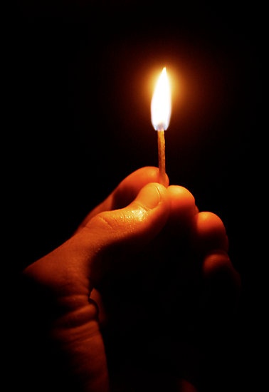 a person holding a lit candle in their hand with the light on it's tip