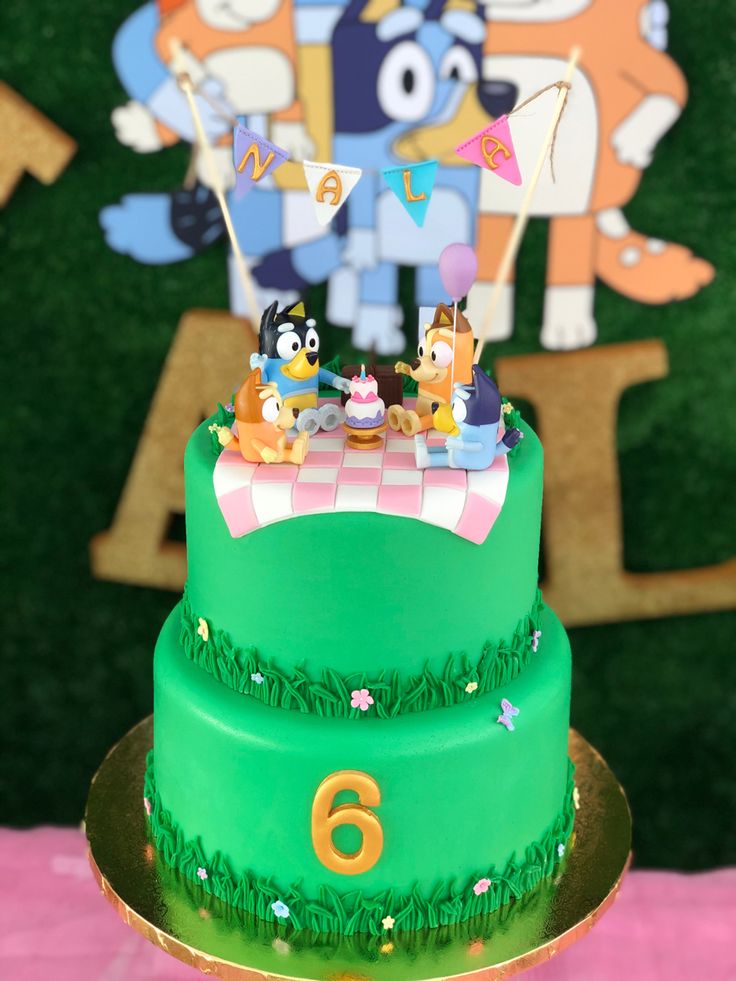 a green cake with cartoon characters on it sitting in front of a pink tablecloth