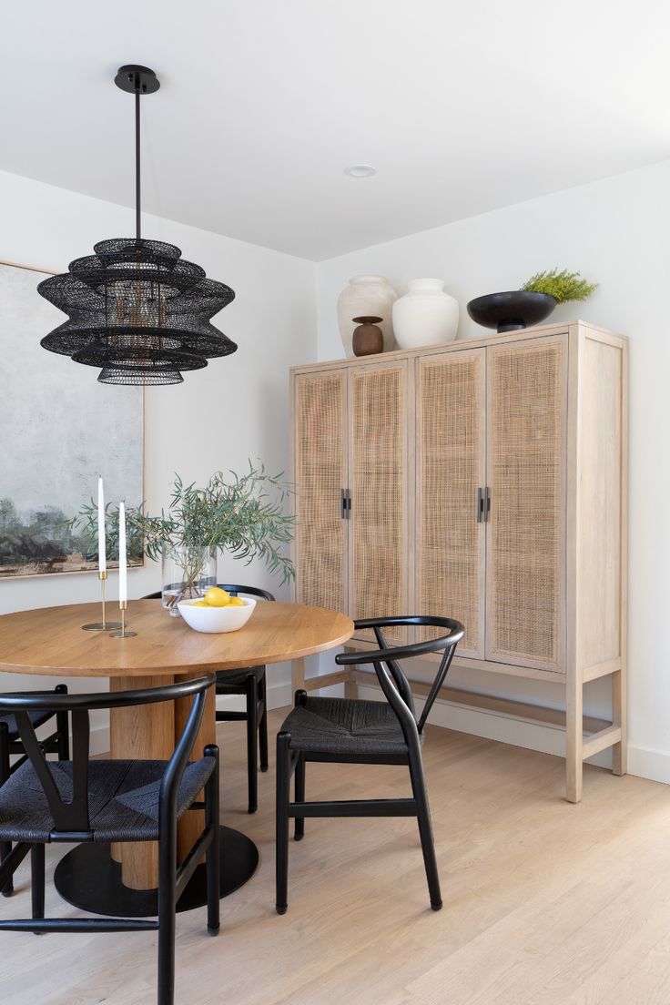 a dining room table and chairs in front of a cabinet with two vases on it