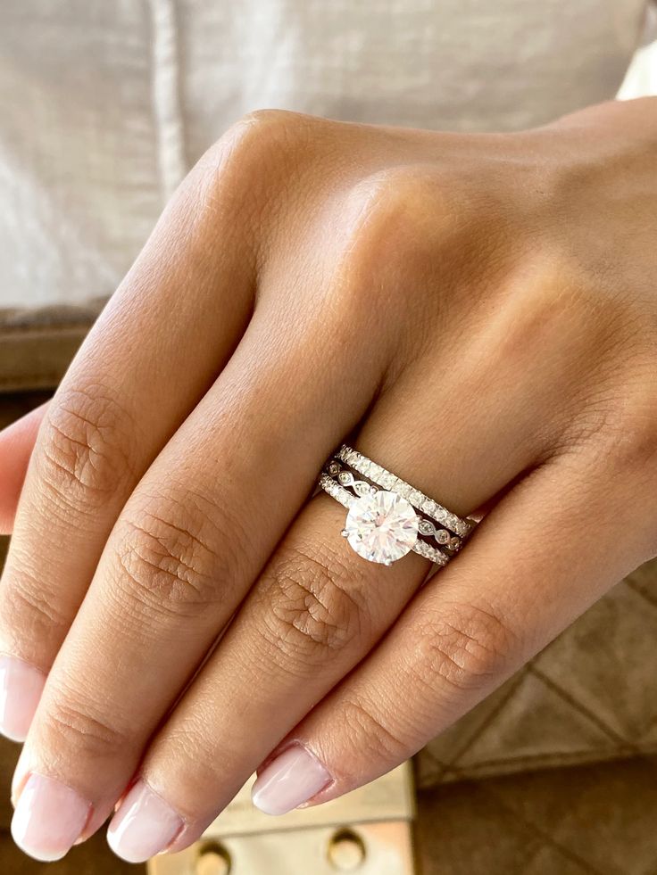 a woman's hand with two wedding rings on her left and the other hand holding an engagement ring