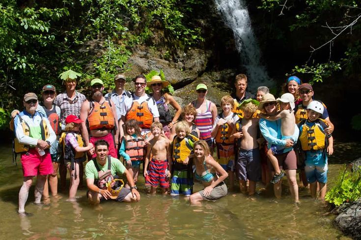 a group of people standing next to each other in the water near a waterfall and trees