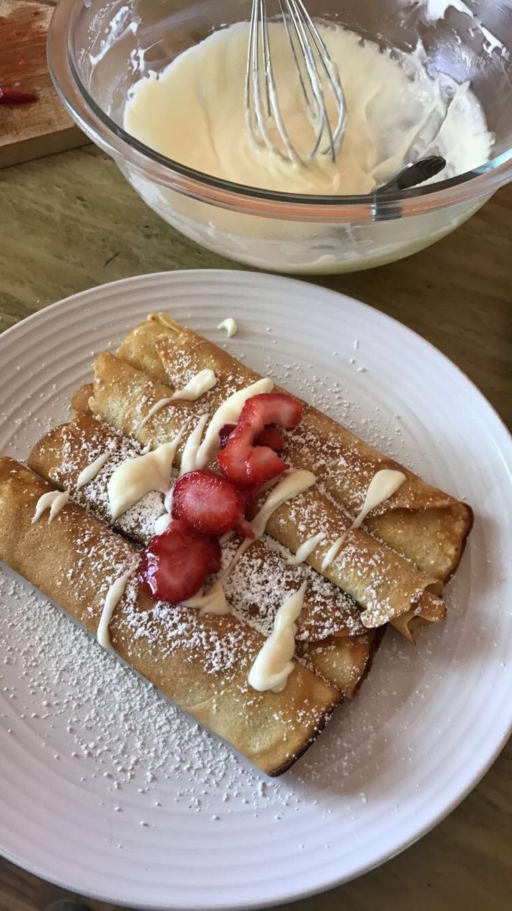 a white plate topped with crepes covered in powdered sugar and strawberries