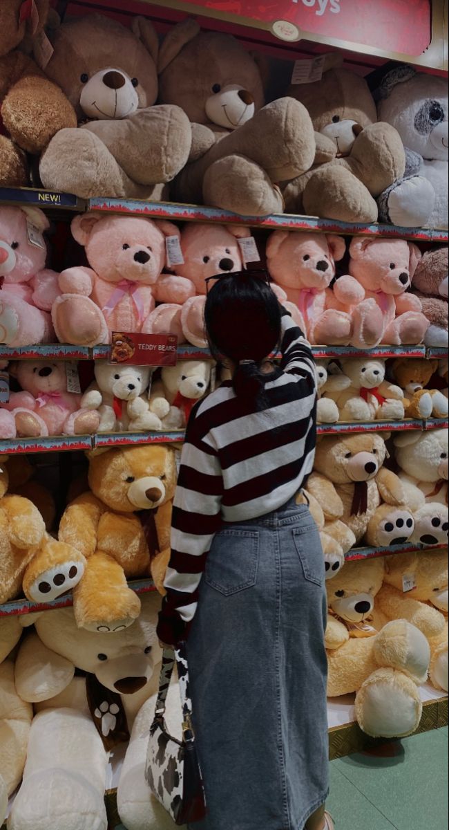 a woman standing in front of a rack of teddy bears and other stuffed animals at a store