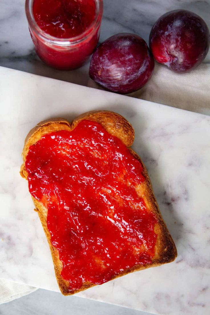 a piece of bread with jam on it next to two plums and a jar of jelly