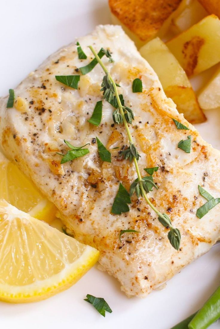 a white plate topped with fish, potatoes and lemon wedges next to green beans