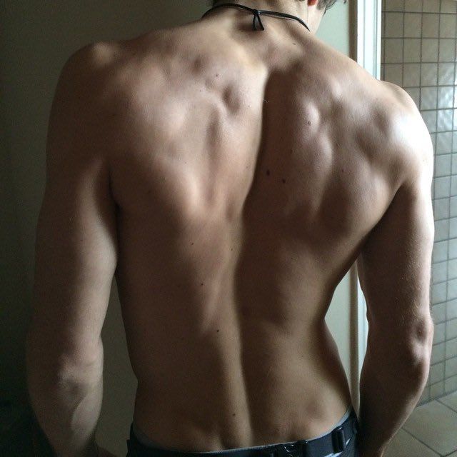 a man with no shirt standing in front of a bathroom mirror looking at his back