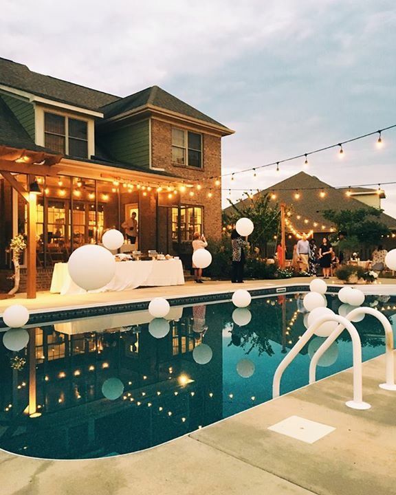 an outdoor pool decorated with white balloons and string lights