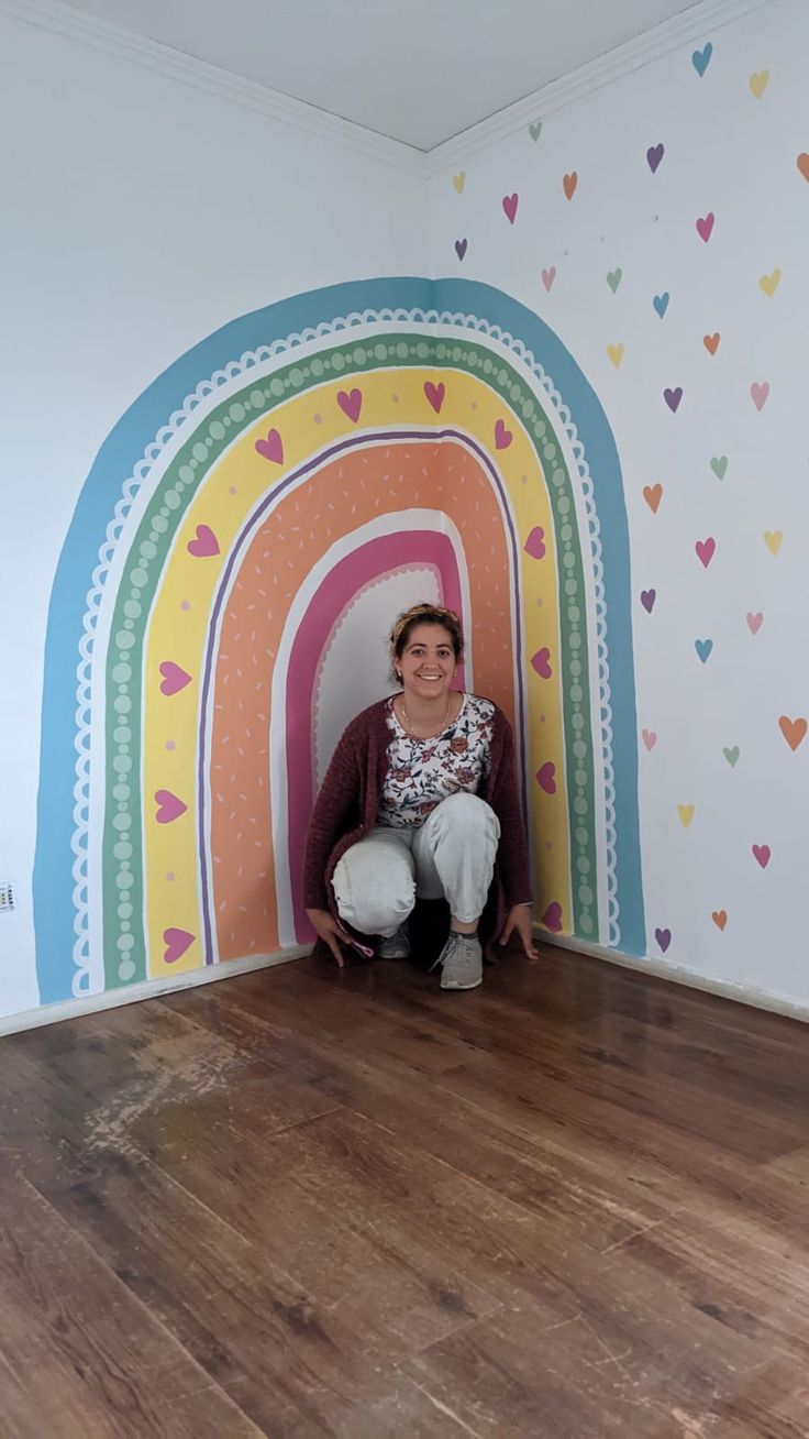 a woman sitting on the floor in front of a rainbow painted wall